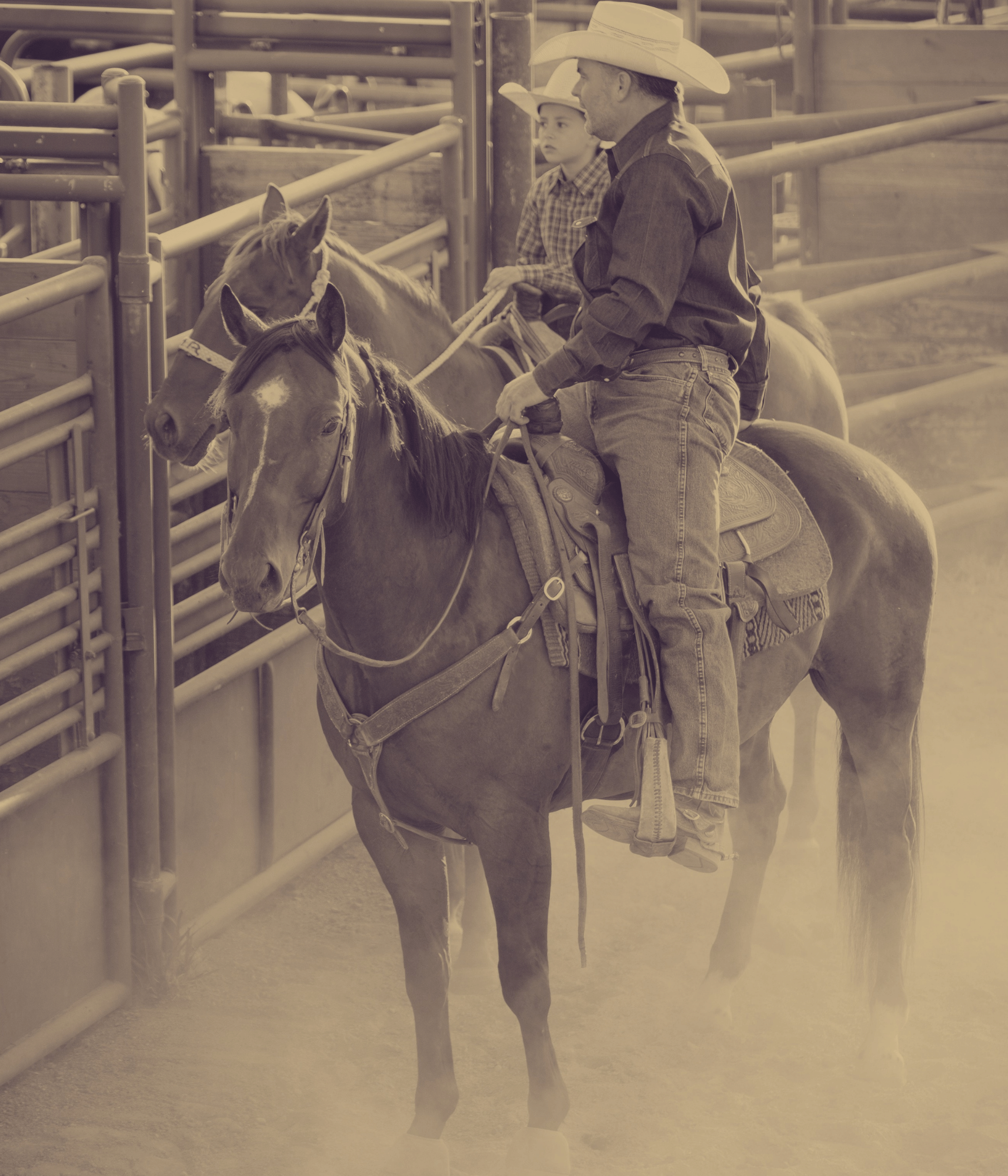a cowboy and a boy on horses in front of rodeo chutes